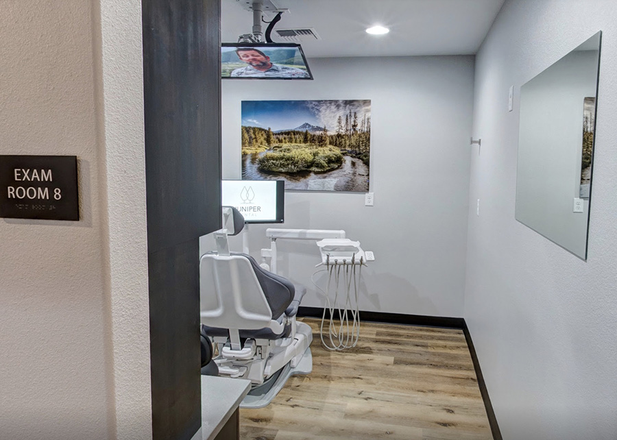 A treatment room; a dental chair, the walls painted a calming blue, wall art featuring nature, a tv hangs from the ceiling